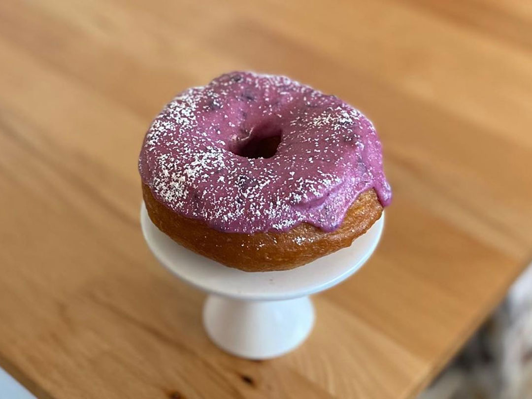 Blueberry donut with a dusting of some powdered sugar on white pedestal stand