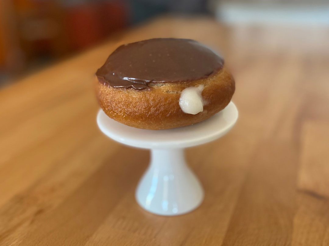 Vanilla custard filled glazed in chocolate donut on white pedestal stand