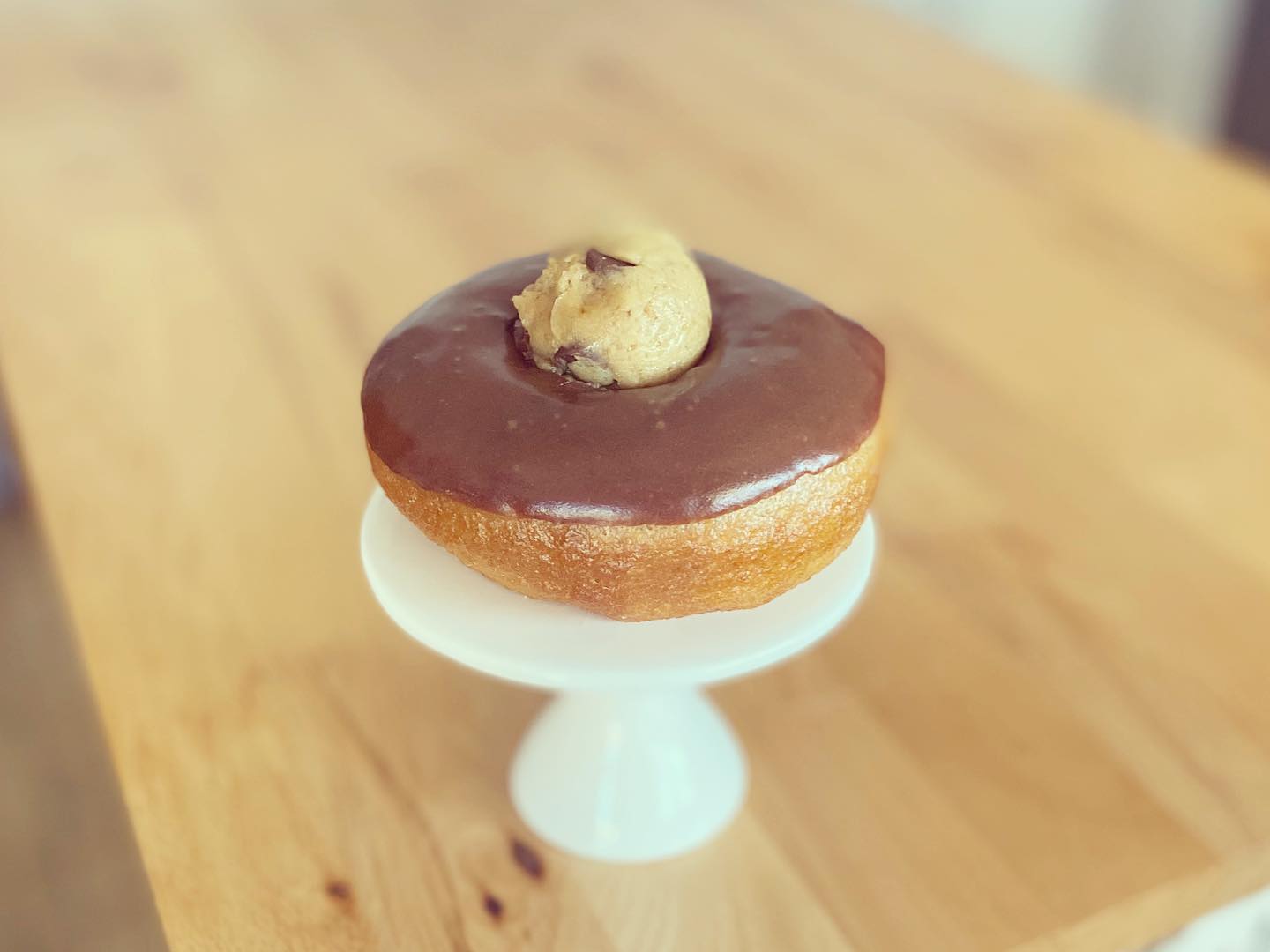 Chocolate covered donut with cookie dough in the middle on white pedestal stand