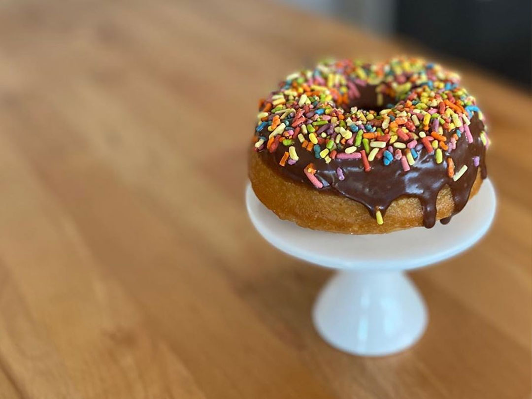 Chocolate donut with some sprinkles on white pedestal stand